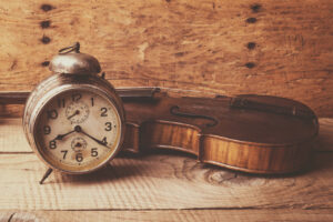 Antique clock and old violin over vintage wooden table