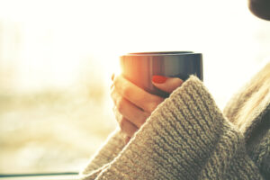 hands holding hot cup of coffee or tea in morning sunlight